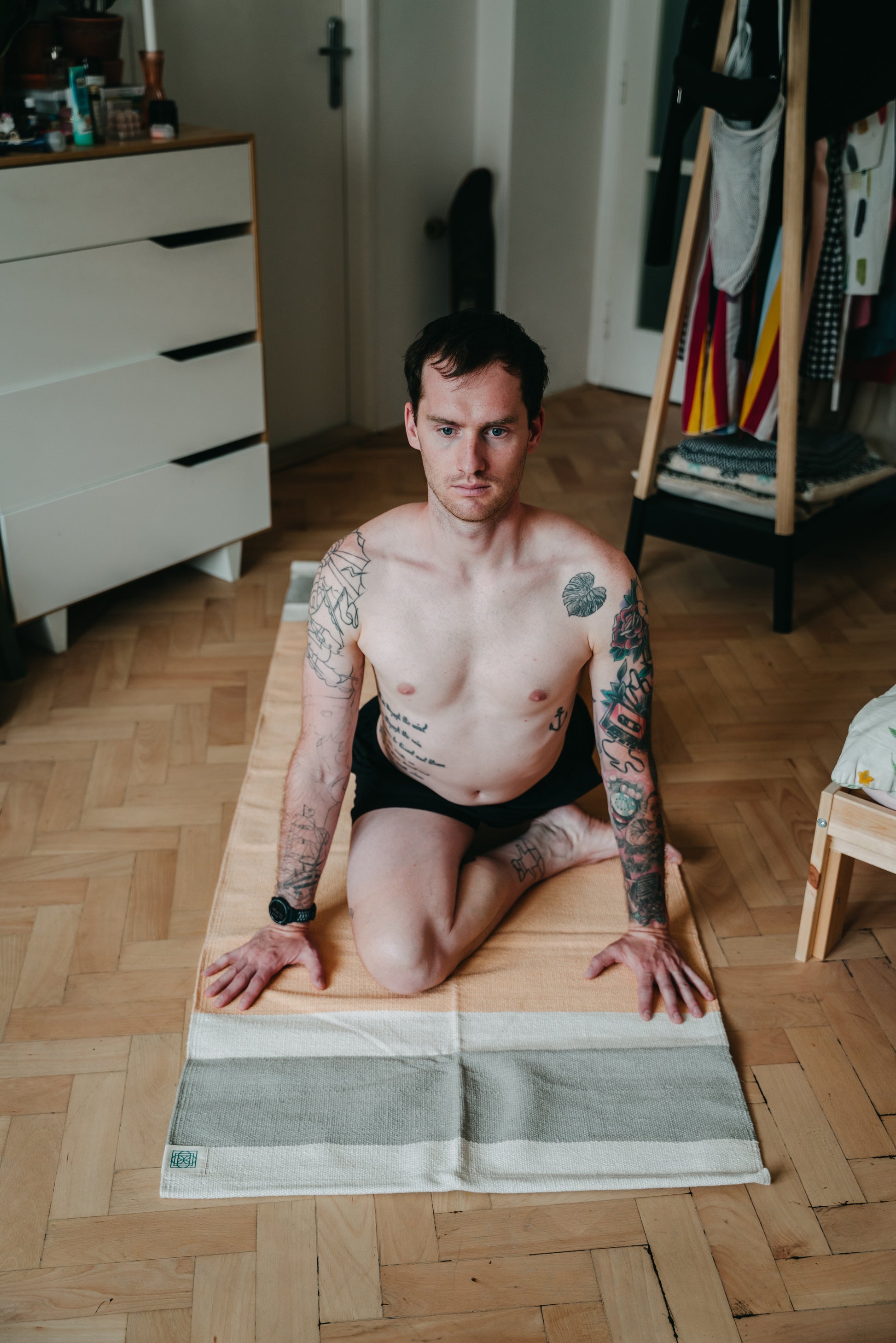 Young man is opening the hips on cotton yoga rug on wooden floor at home