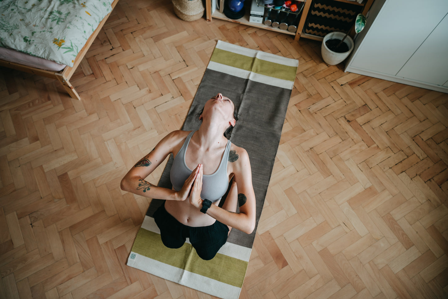 Yogi practicing ustrasana (camel pose) on cotton yoga rug on wooden floor in her room. 