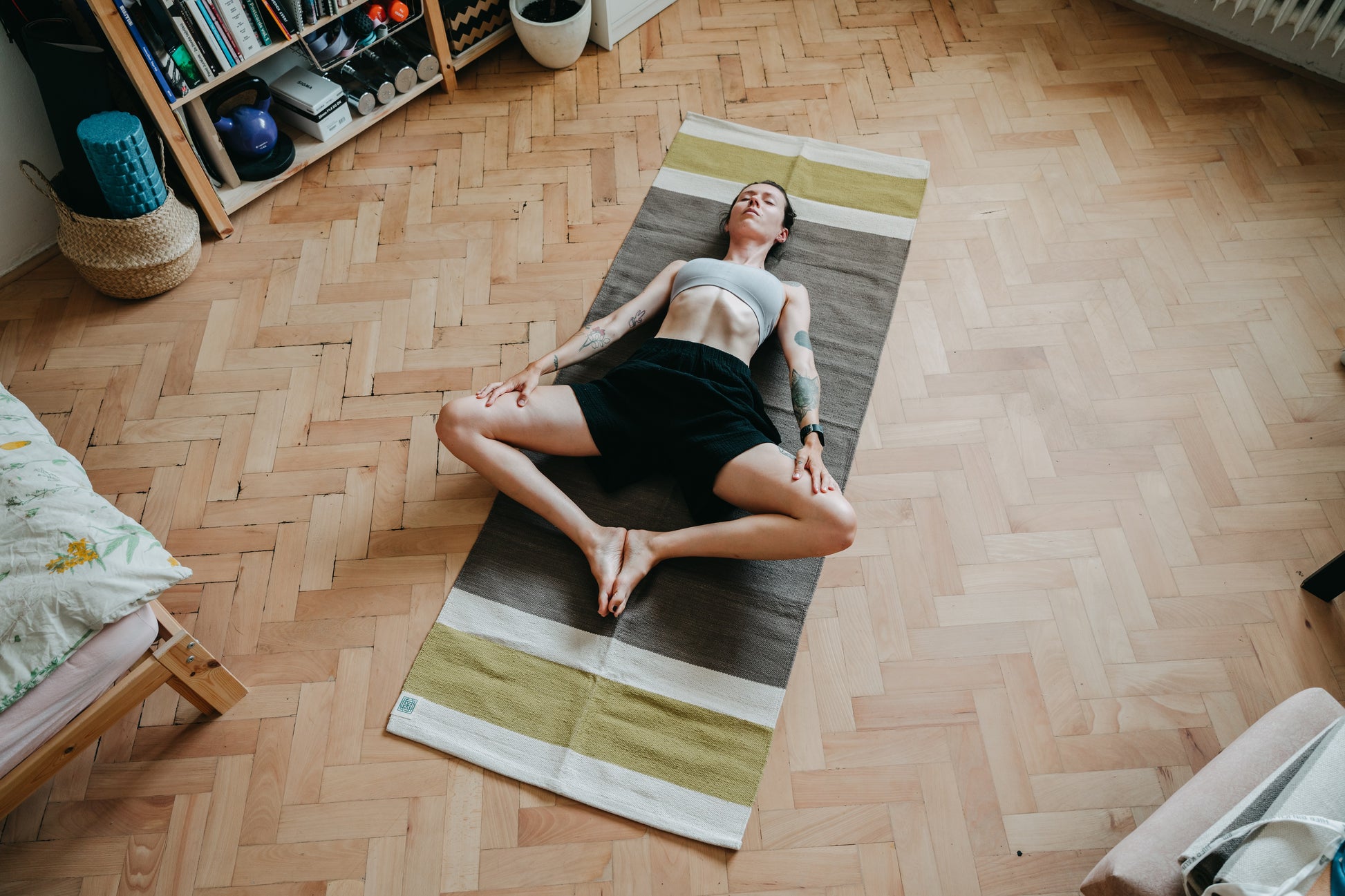 Yogi practicing opening her hips (bound angle pose) on cotton yoga rug on wooden floor in her room. 
