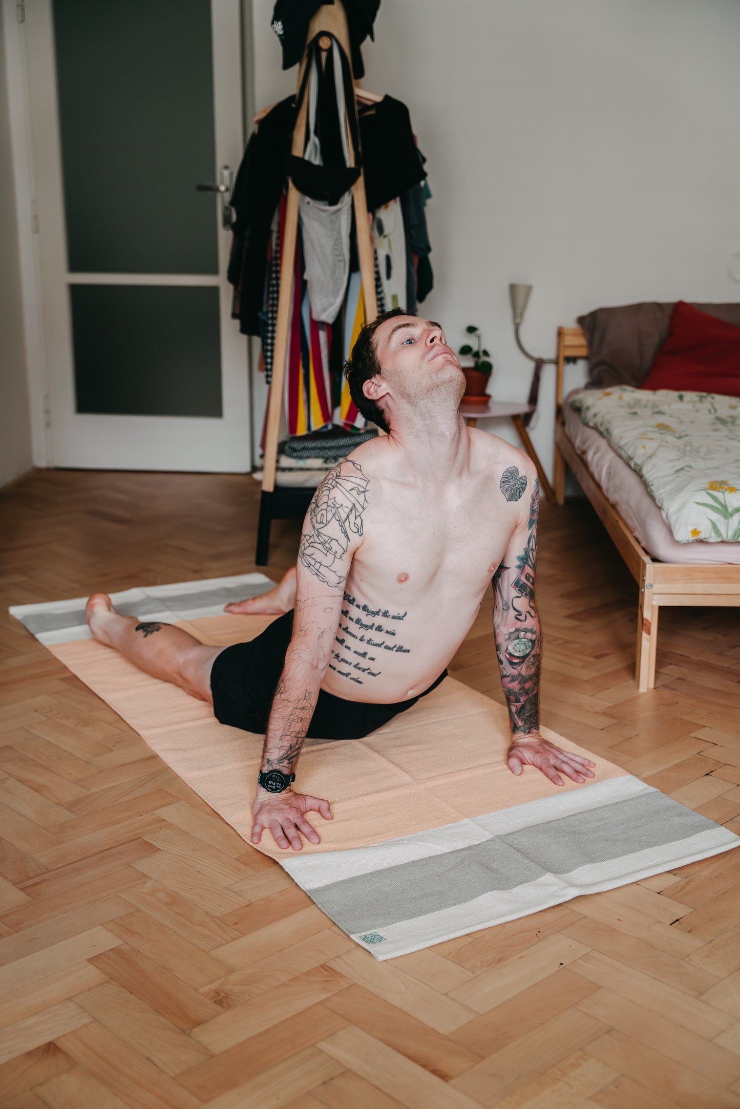 Young man is practicing upward facing dog on cotton yoga rug on wooden floor at home